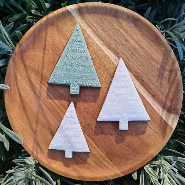 3 Christmas tree cookies in green and white with Christmas themed text embosser on a wooden plate