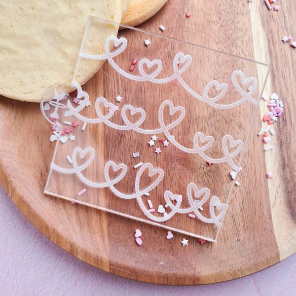 embosser with heart line designs on a wooden plate with cookies and valentines sprinkles